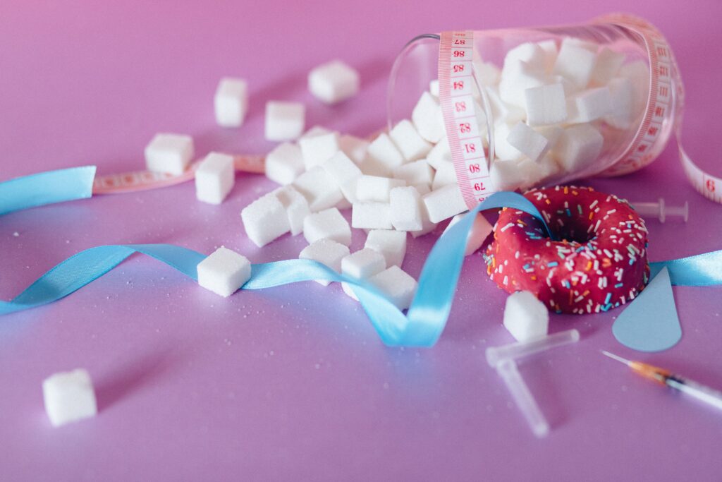 Creative representation of sugar consumption using cubes, donut, ribbon, and syringe.